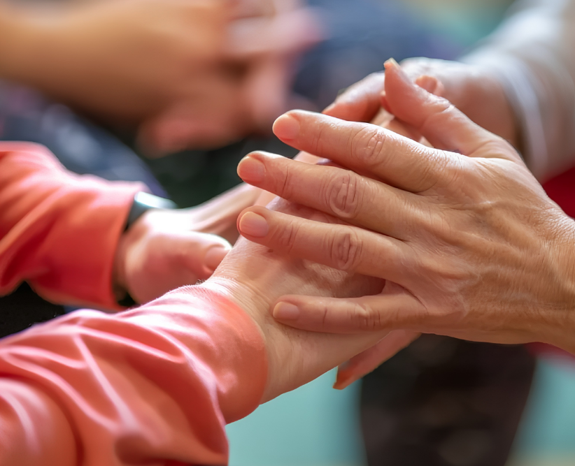 A diverse group of individuals standing in a circle, holding hands, symbolizing unity and support in aged care.