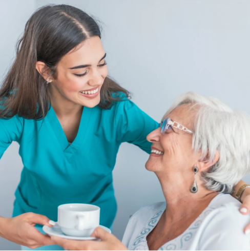  A nurse offers a cup of coffee to an elderly woman, showcasing support and care in a home setting.
